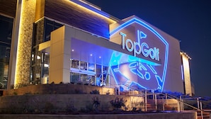 A modern building with a neon sign reading "TopGolf" and a visible entrance with steps.