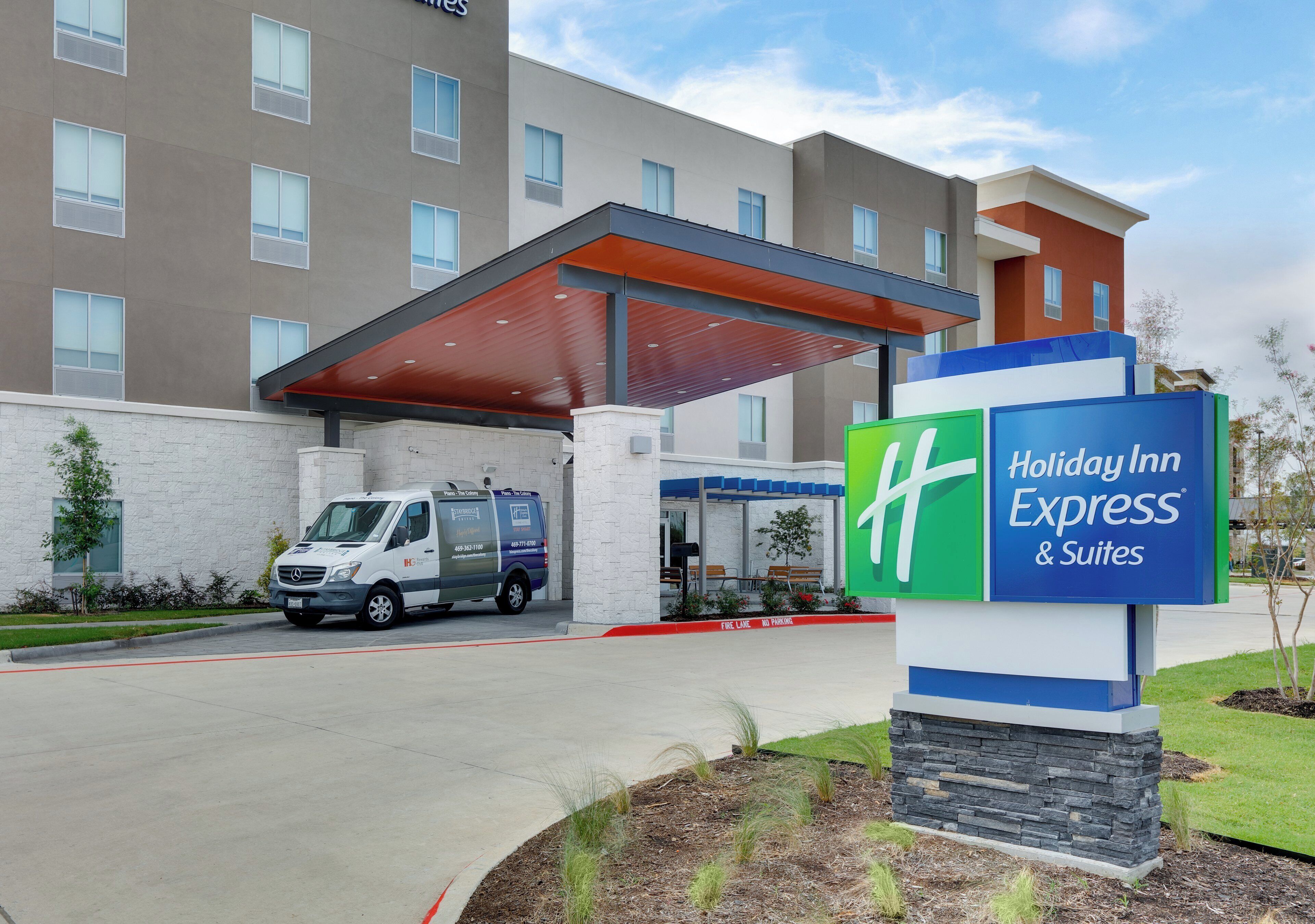 Un Holiday Inn Express & Suites con entrada cubierta, un área de estacionamiento y un edificio con múltiples ventanas.