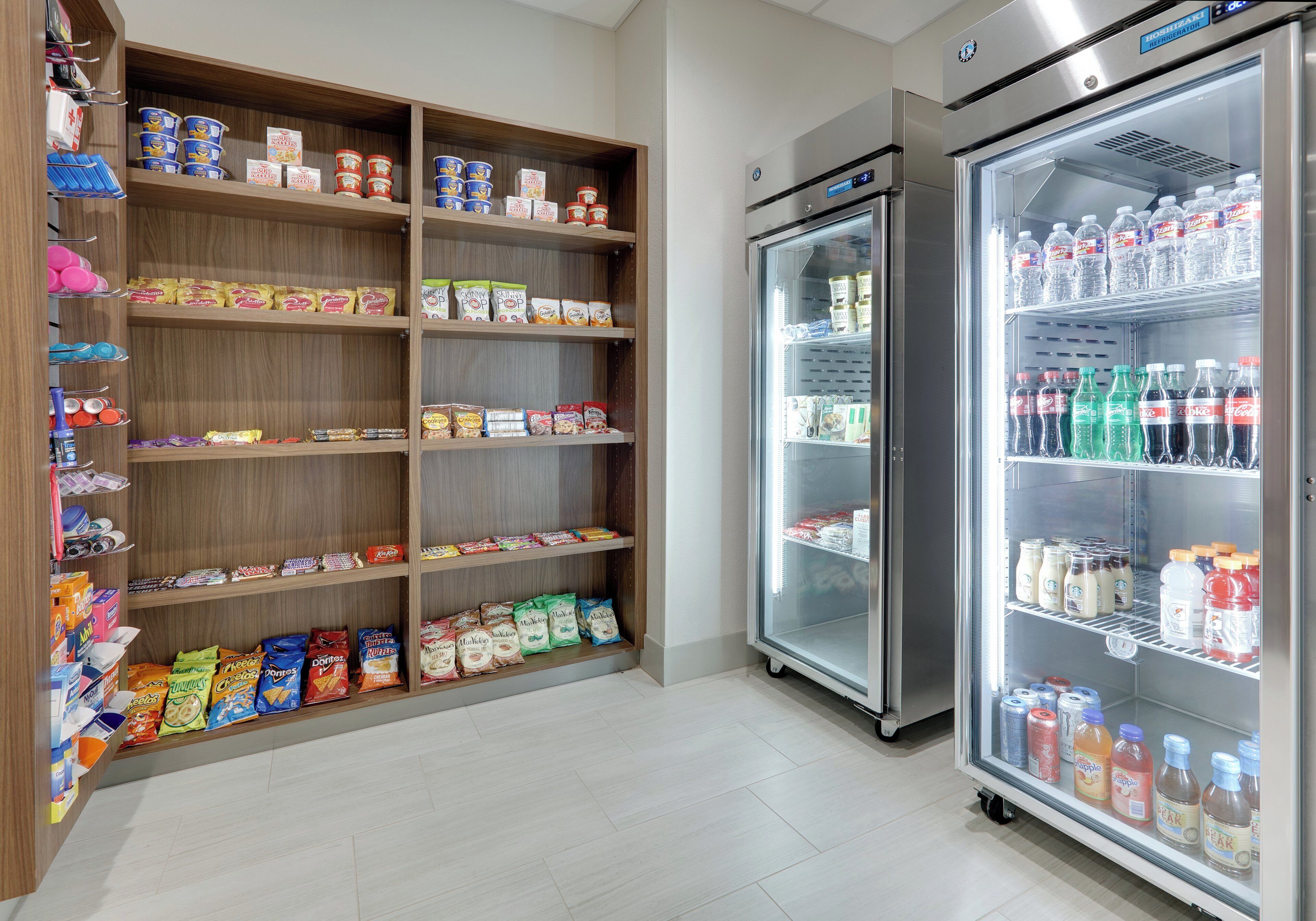 A refrigerated display case stocked with bottled water and soft drinks, adjacent to a pantry stocked with snacks and condiments.