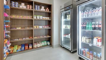 A refrigerated display case stocked with bottled water and soft drinks, adjacent to a pantry stocked with snacks and condiments.