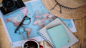 A world map, a pair of glasses, a straw hat, a notebook, and a coffee cup on a wooden surface. - Holiday Inn Express & Suites Plano - The Colony by IHG (The Colony)