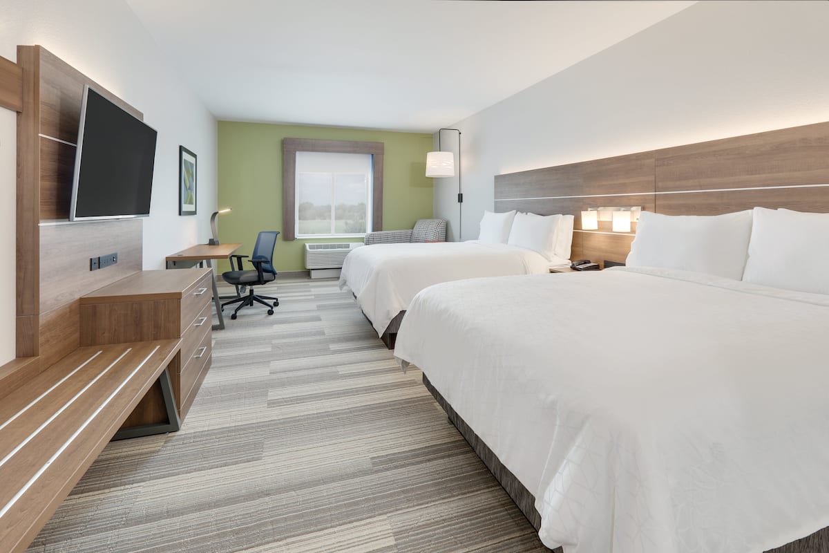 A hotel room with two beds, a desk, a chair, a TV, and a window.