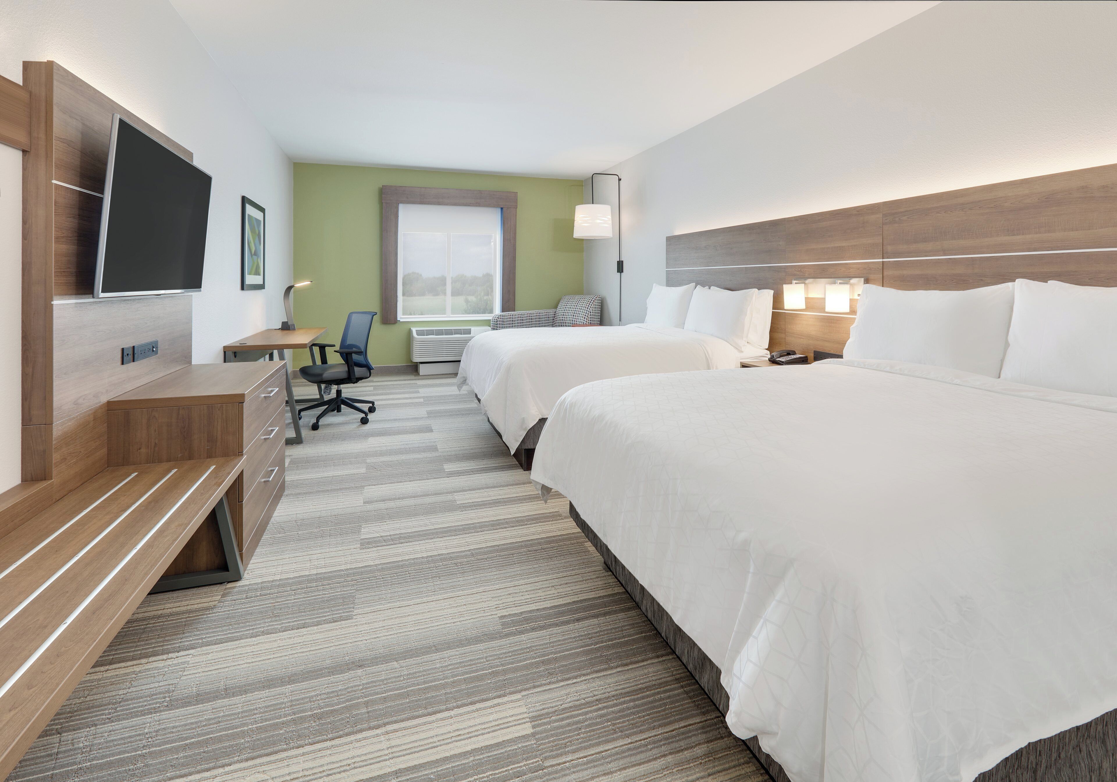 Een hotelkamer met twee bedden, een bureau, een stoel, een televisie en een raam met uitzicht.