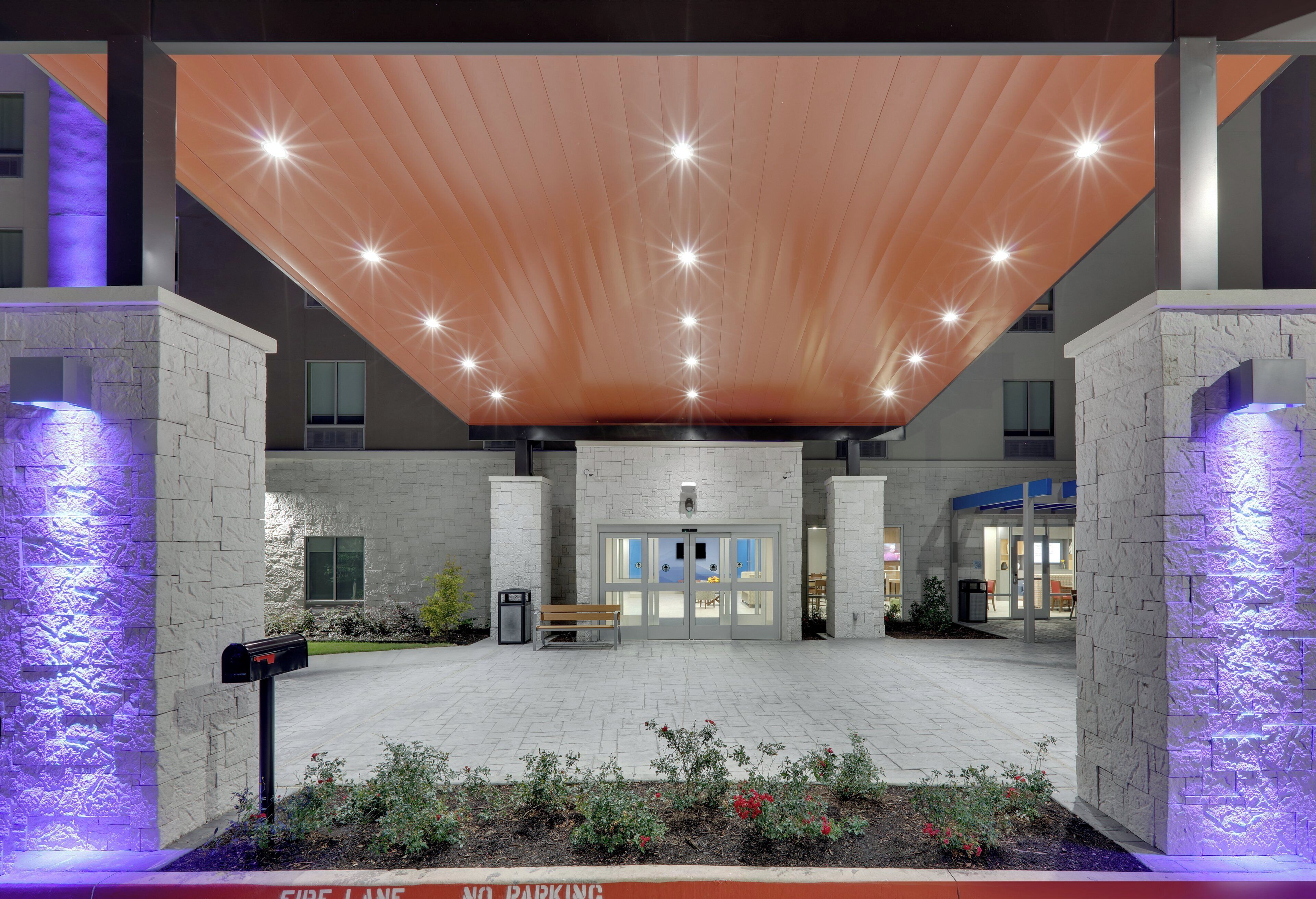 A modern building entrance with a sloped roof, a fire lane, and a gated entrance.