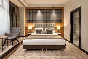 Une chambre d’hôtel avec un grand lit, deux tables de chevet avec des lampes, une chaise et une grande fenêtre avec des rideaux.