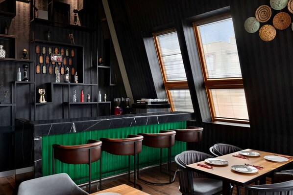 Un espace bar moderne avec un mur d’accent vert, un comptoir en bois et de nombreux tabourets.
