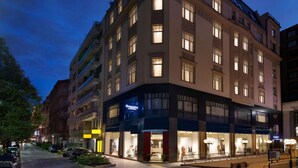 Un hôtel à plusieurs étages, avec une entrée d’angle, de grandes fenêtres et une devanture bien visible.