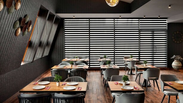 Un restaurant moderne avec des tables en bois, des chaises noires et une grande fenêtre équipée de stores.