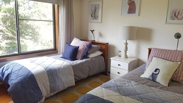 Une chambre avec deux lits, une table de chevet, une lampe et des œuvres d’art encadrées accrochées au mur.