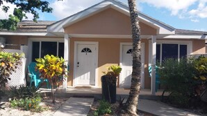 Einbungalow mit sandfarbener Fassade, zwei Hauseingängen und einer kleinen Veranda mit einer Palme.