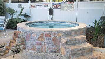 A stone hot tub surrounded by a white fence with various warning signs.