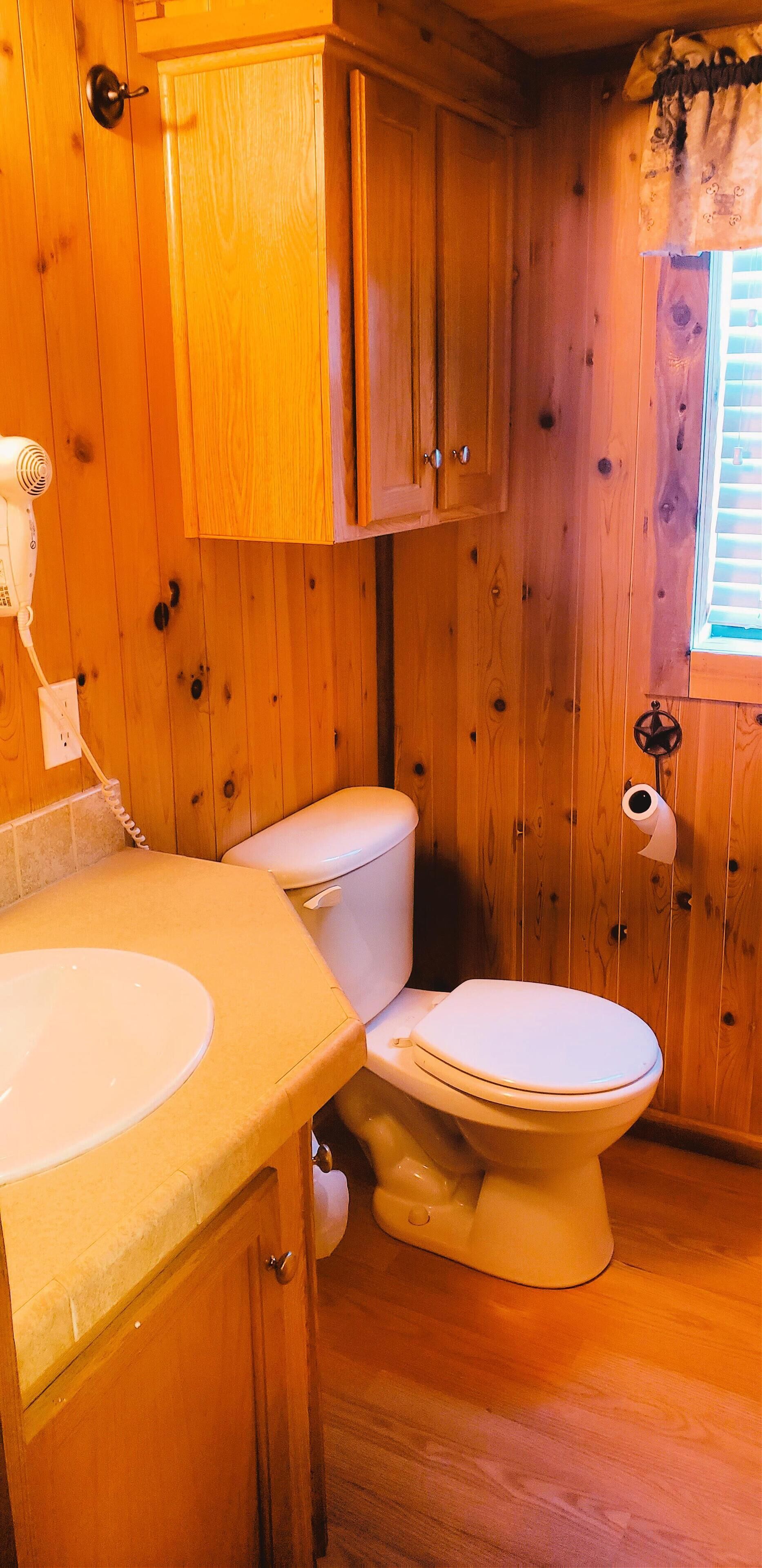 Baño de cabaña de madera con inodoro, lavabo y ventana con persianas.