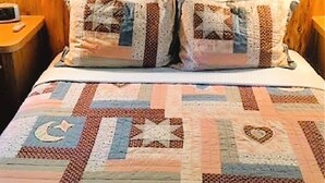A wooden cabin interior with a bed featuring a quilted bedspread and two pillows.