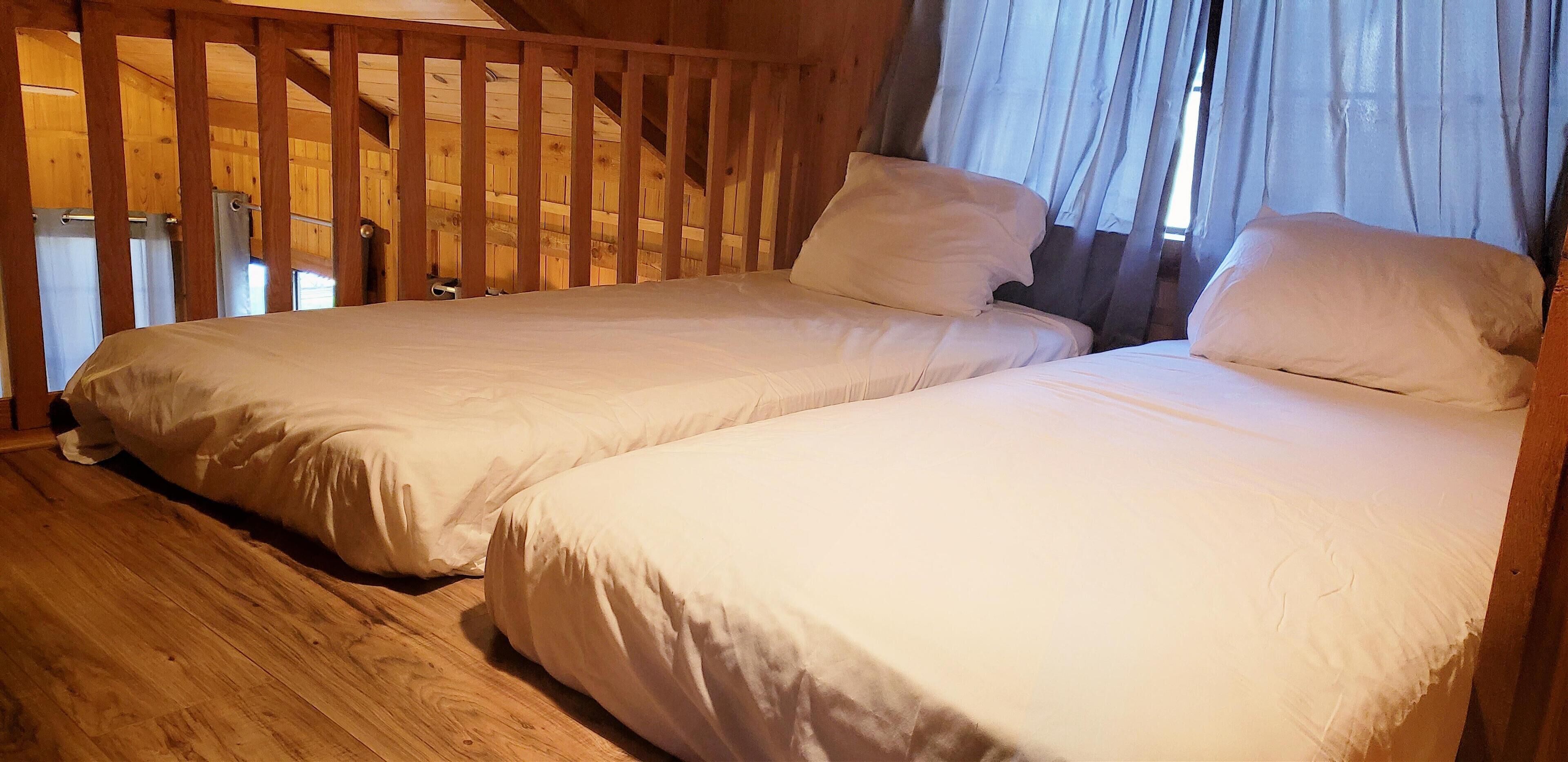 Une chambre avec deux lits simples, un plancher en bois et une fenêtre avec des rideaux.