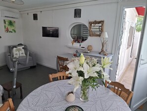 Un comedor con una mesa redonda, sillas, un florero con flores y un espejo colgado en la pared.
