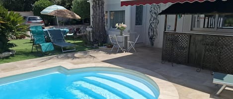 A swimming pool with a stone deck, outdoor seating, and a bar area.