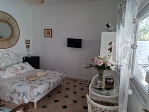 Un dormitorio con cama, mesita de noche, televisor, espejo y ventana con cortinas.