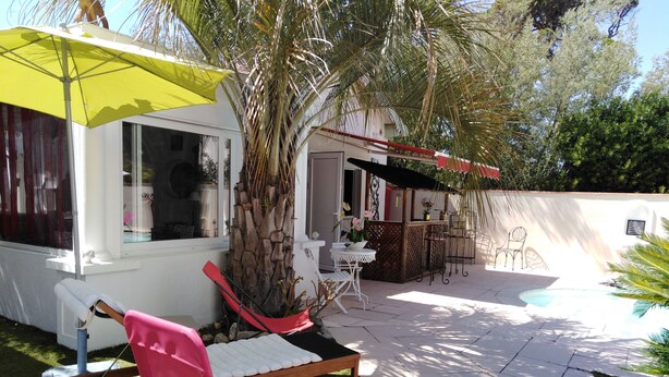 A patio area with a pool, a pink chair, a yellow umbrella, and a small table. - Small 30m2 house for 2 people on private property with swimming pool (Fréjus)