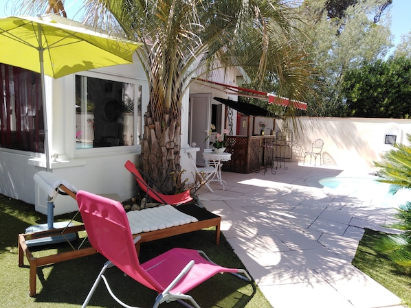 Uma área de pátio com piscina, uma cadeira rosa, um guarda-sol amarelo e uma mesa pequena.