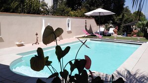 A swimming pool with a curved edge, surrounded by a low wall, and potted plants in the foreground. - Small 30m2 house for 2 people on private property with swimming pool (Fréjus)