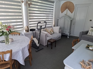 A room with a dining table, a sofa, a chair, a small table, and a wall-mounted fan.