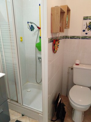 A bathroom with a glass-enclosed shower, a toilet, and a small wooden cabinet. - Small 30m2 house for 2 people on private property with swimming pool (Fréjus)