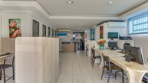 A modern hotel lobby with a long reception desk, multiple seating areas, and a visible kitchen in the background. - Marazul Apart Hotel (Florianópolis)