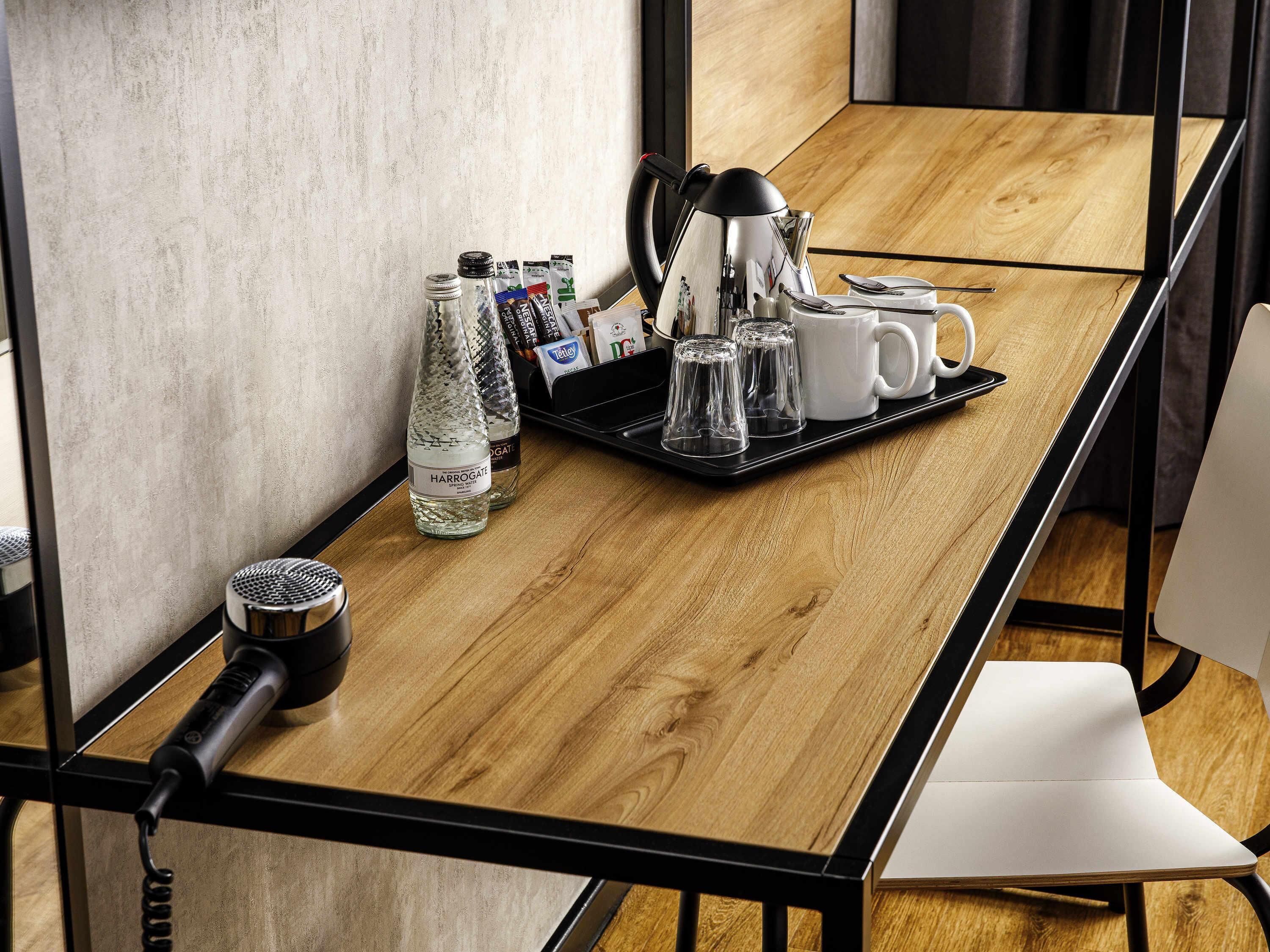 A wooden table with a tray holding a kettle, cups, and condiments.