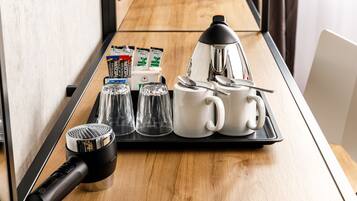 Un plateau de petit-déjeuner avec une machine à café, des tasses, des verres et un sèche-cheveux, posé sur une table en bois.