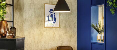 Una habitación con una mesa redonda de madera, cuatro sillas, una lámpara colgante, una obra de arte enmarcada y una puerta azul.