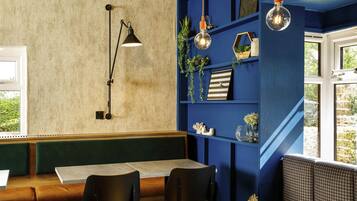 Een zithoek met een tafel en stoelen, een boekenkast met decoratieve objecten, en een hanglamp.