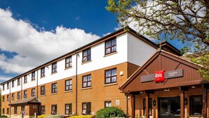 A hotel with a modern design, featuring a mix of brick and white exterior walls, multiple windows, and a prominent red and white sign for the ibis hotel. - ibis Wakefield East-Castleford (Castleford)