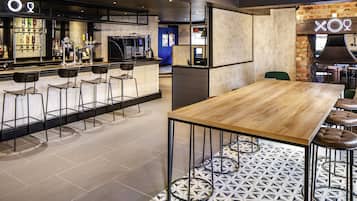 Zona de bar moderna con barra, taburetes y un espacio de estar con mesa y sillas de madera.