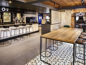 Zona de bar moderna con barra, taburetes y un espacio de estar con mesa y sillas de madera.