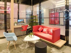 Un hall d’hôtel moderne avec un canapé rouge, une table blanche, une chaise bleue et un écran d’ordinateur.