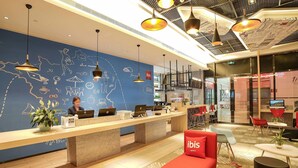 A hotel reception area with a blue wall featuring travel-related illustrations, a reception desk with laptops, and red seating. - Ibis Chengdu Hi-Tech Zone Longhu Hotel (Chengdu)
