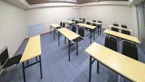 A conference room with multiple tables and chairs, a sloped ceiling with lighting, and a vent on the wall.