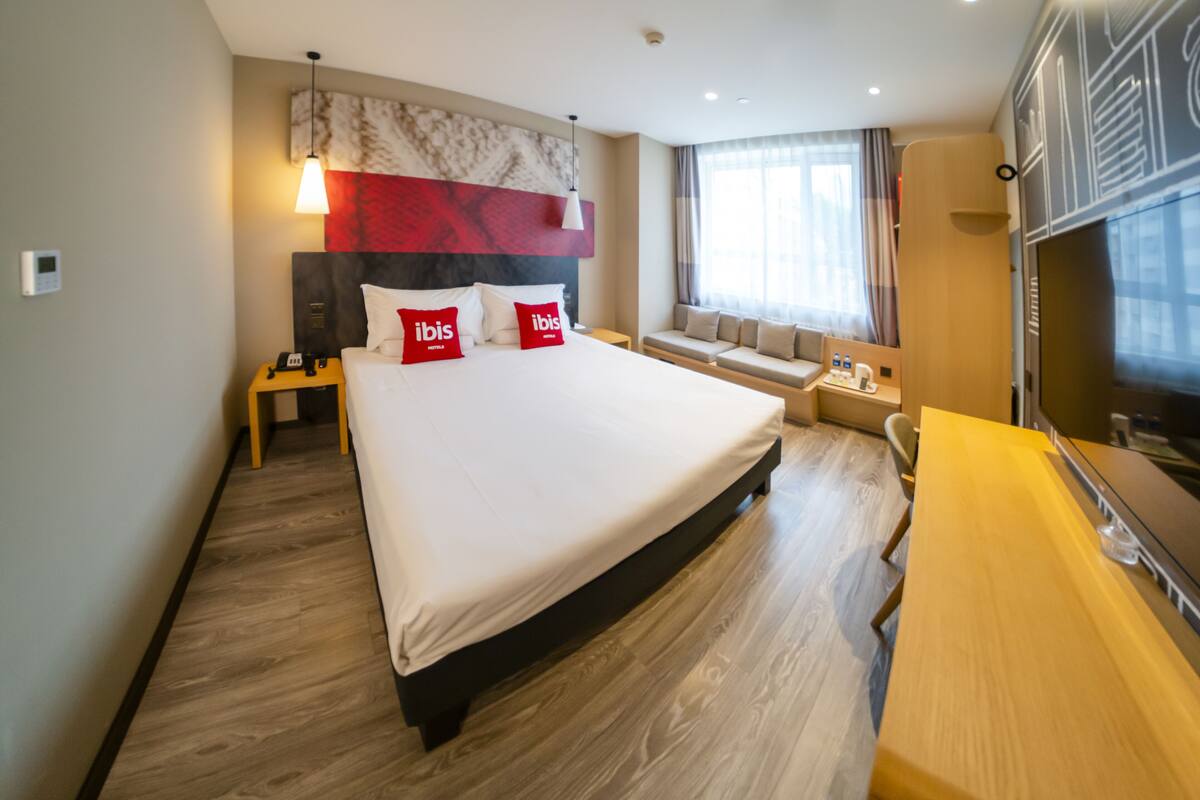 Een hotelkamer met een groot bed, een nachtkastje, een bureau, een televisie en een raam met gordijnen.