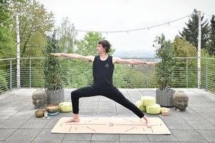 Eine Person führt eine Yoga-Pose auf einer Matte im Freien mit einem malerischen Ausblick im Hintergrund aus.