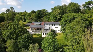 A large white house with a red roof, surrounded by dense green trees. - Habitat Esslingen (Esslingen)