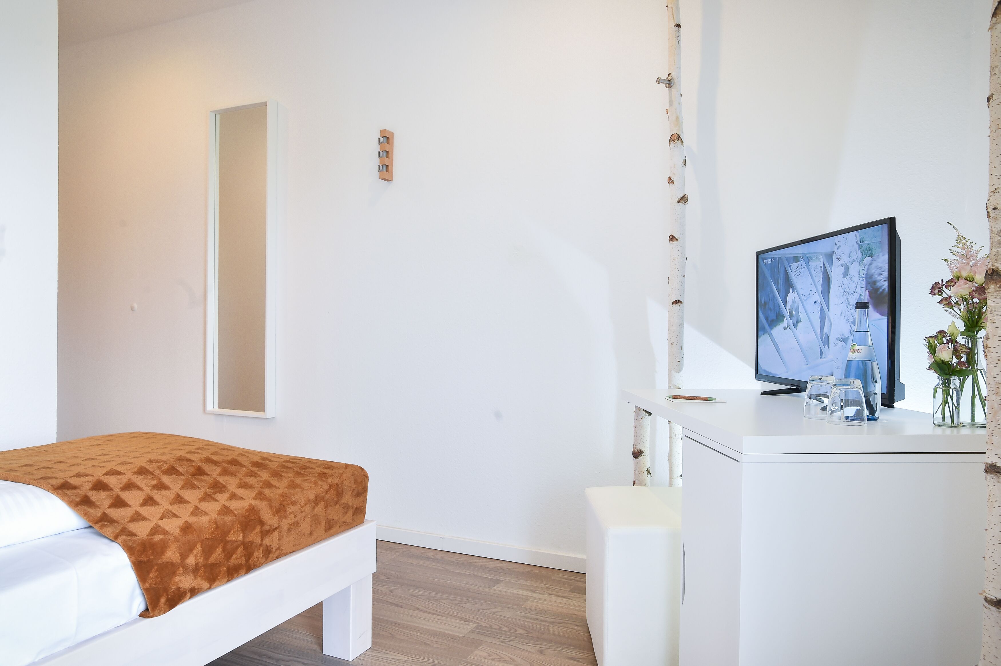 Een hotelkamer met een bed, een bureau, een televisie en een vaas met bloemen.