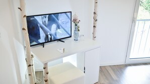A modern room with a flat-screen TV on a white desk, a small vase with flowers, and a wooden floor. - Habitat Esslingen (Esslingen)
