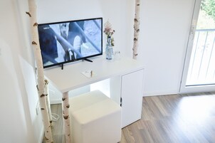 Ein modernes Zimmer mit einem Flachbildfernseher auf einem weißen Schreibtisch, einer kleinen Vase mit Blumen und Holzboden.