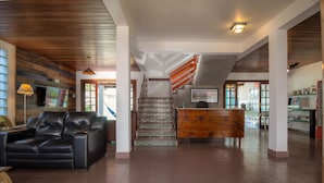 Un hall d’entrée spacieux, avec un canapé en cuir, un comptoir d’accueil en bois et un escalier doté d’une rampe en bois.