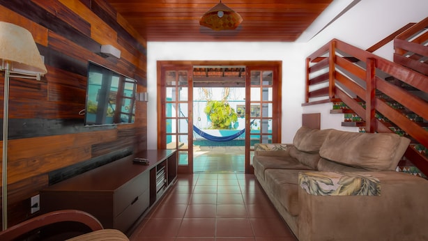 Un salon avec un plafond en bois, un téléviseur fixé au mur, un canapé, une table basse et un hamac à l’arrière-plan.