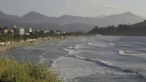 Une plage côtière avec des vagues, des bâtiments et des montagnes en arrière-plan.