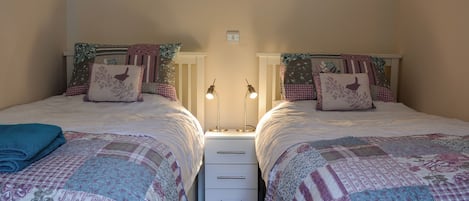 Een tweepersoonskamer met twee bedden, elk voorzien van een nachtkastje, een lamp en een lade.