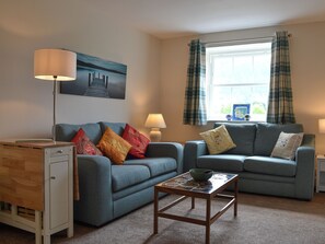 A living room with two sofas, a coffee table, a lamp, a painting, and a window with curtains.
