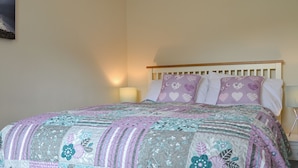 Een bed met een quilt met bloemenprint, een houten hoofdbord en twee bedlampjes.