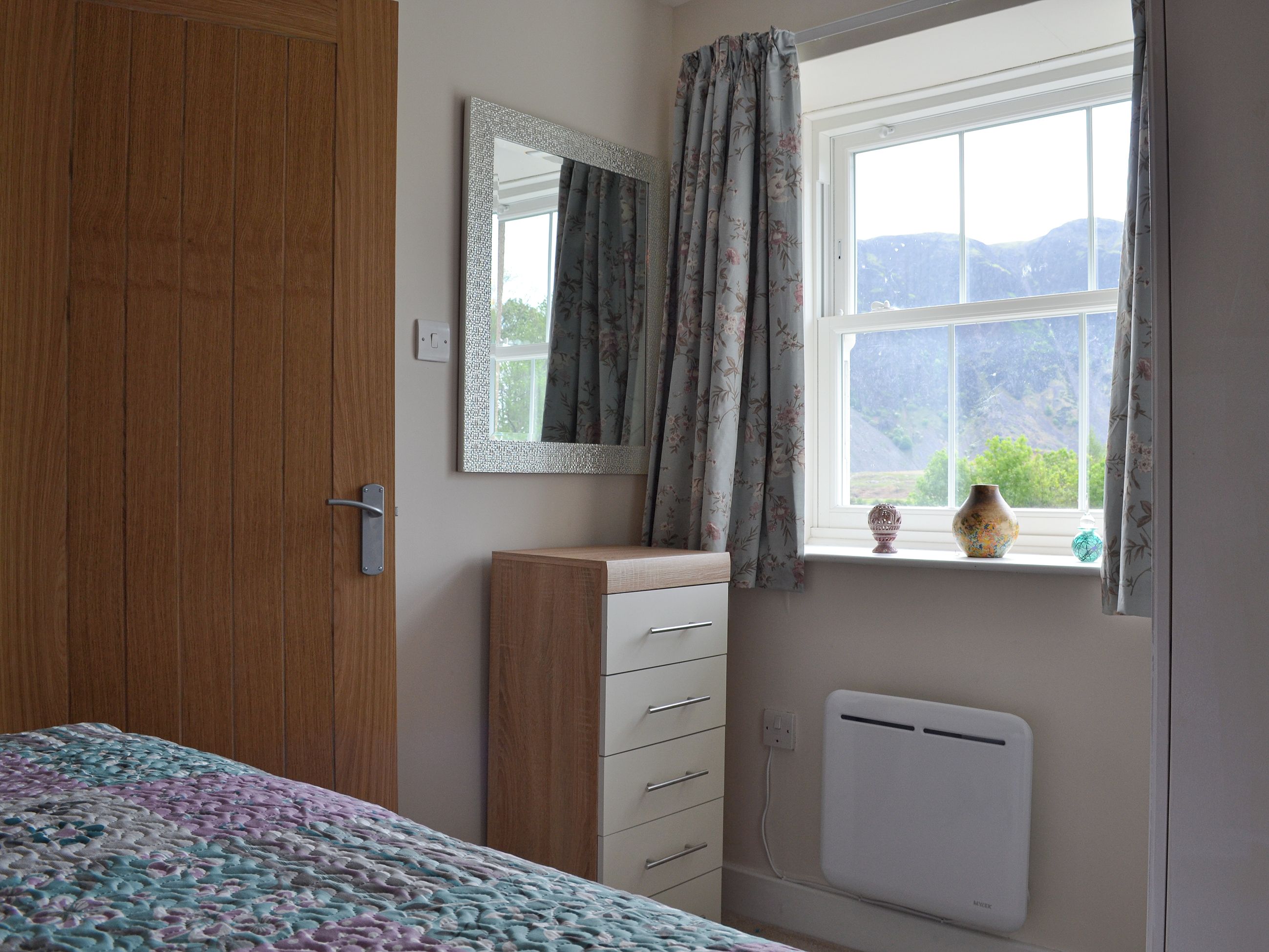 Un dormitorio con un armario de madera, un aparador, un radiador y una ventana con vistas a montañas.